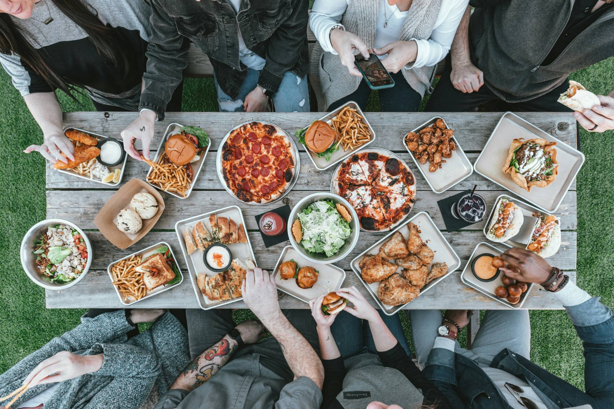 A shared table seen from above, mid-meal, with hands reaching in over the plates
